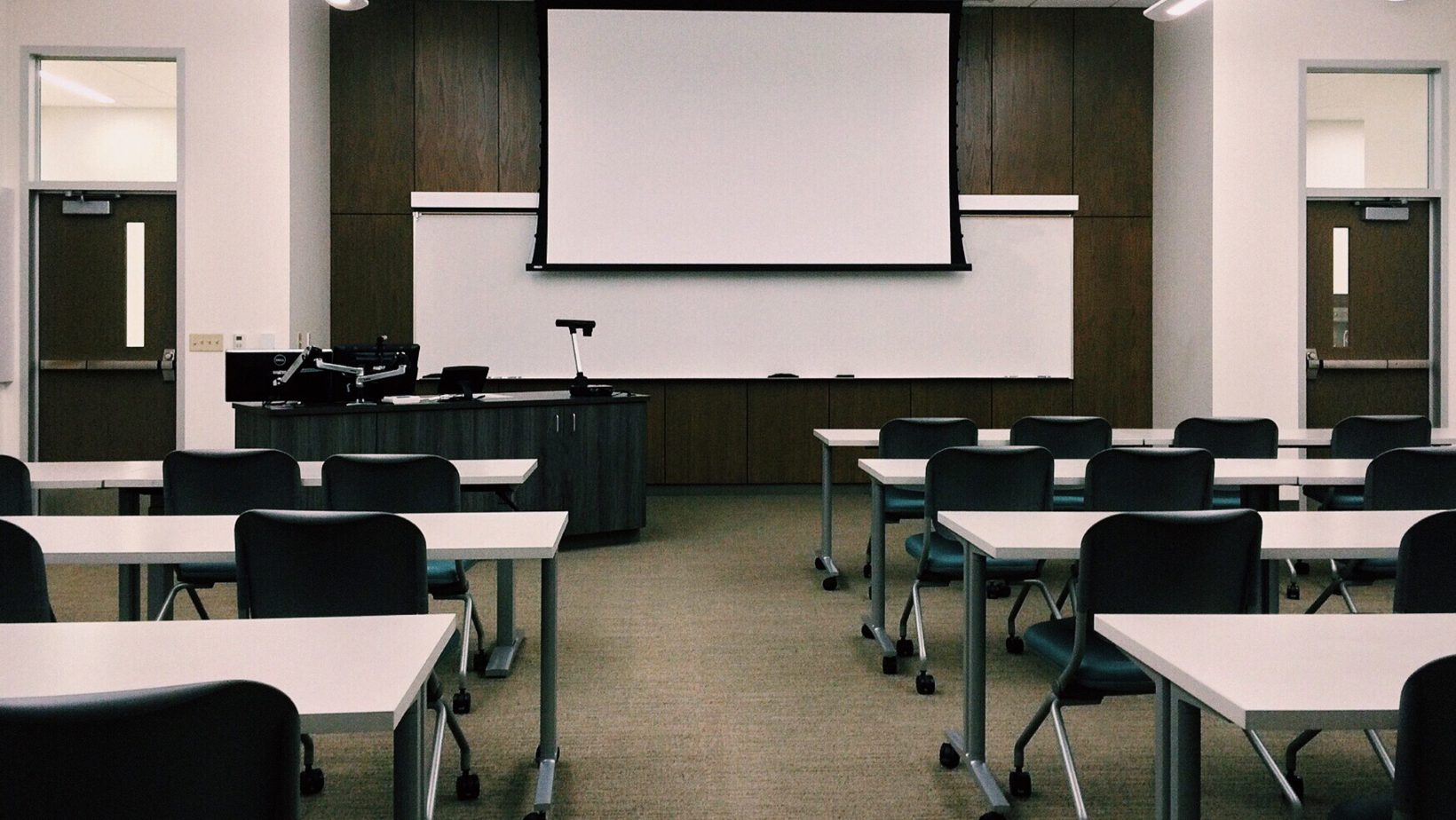 Empty classroom with long tables and chairs and a projector screen
